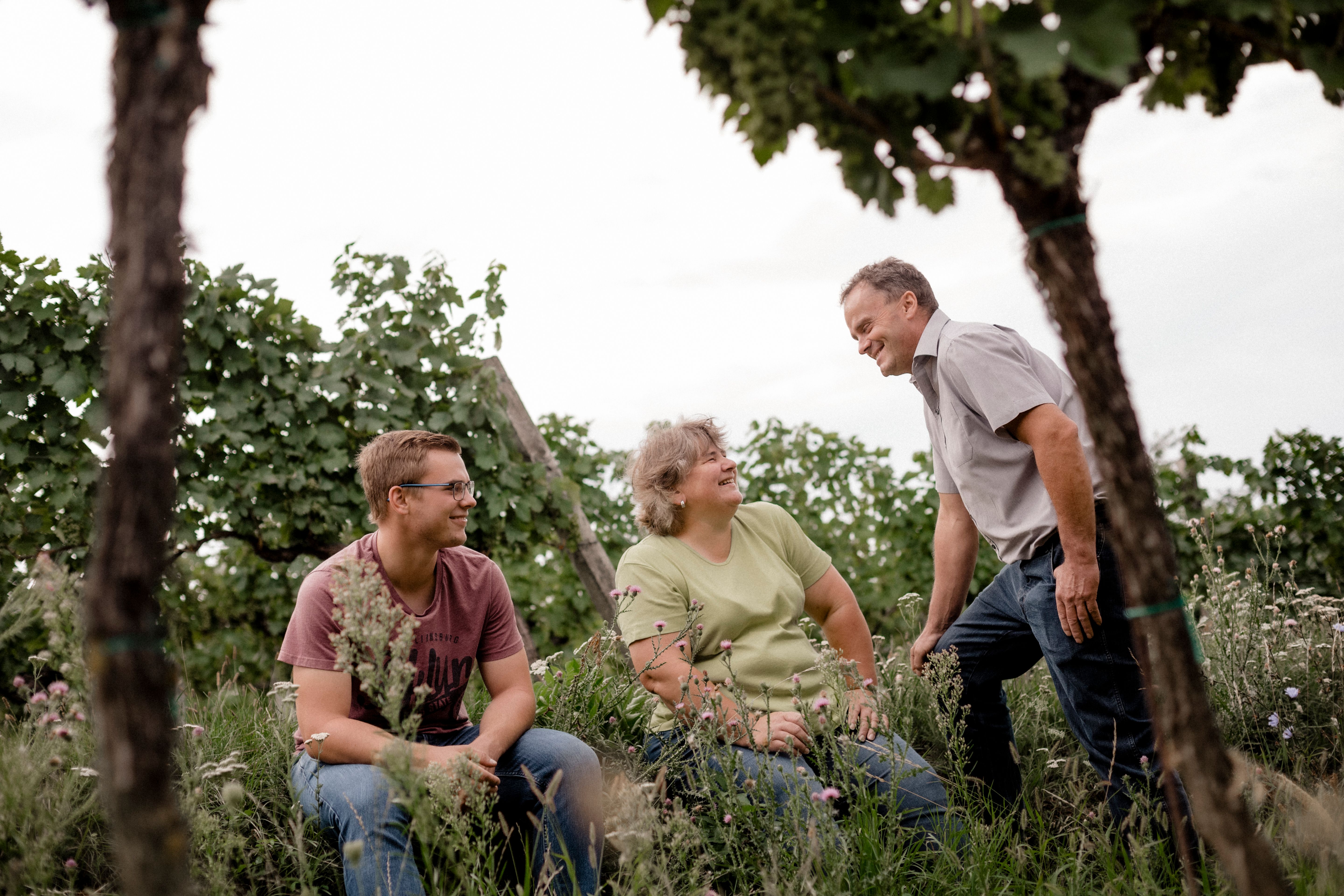 Three people in a vineyard laughing together.