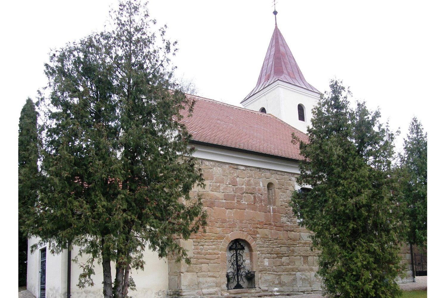 Historische Kirche mit rotem Dach und Turm, umgeben von Bäumen.
