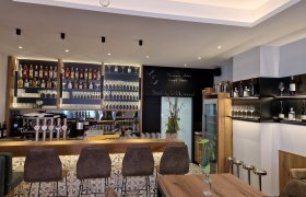 Moderne Bar mit Flaschenregalen, Gläsern und Barhockern.