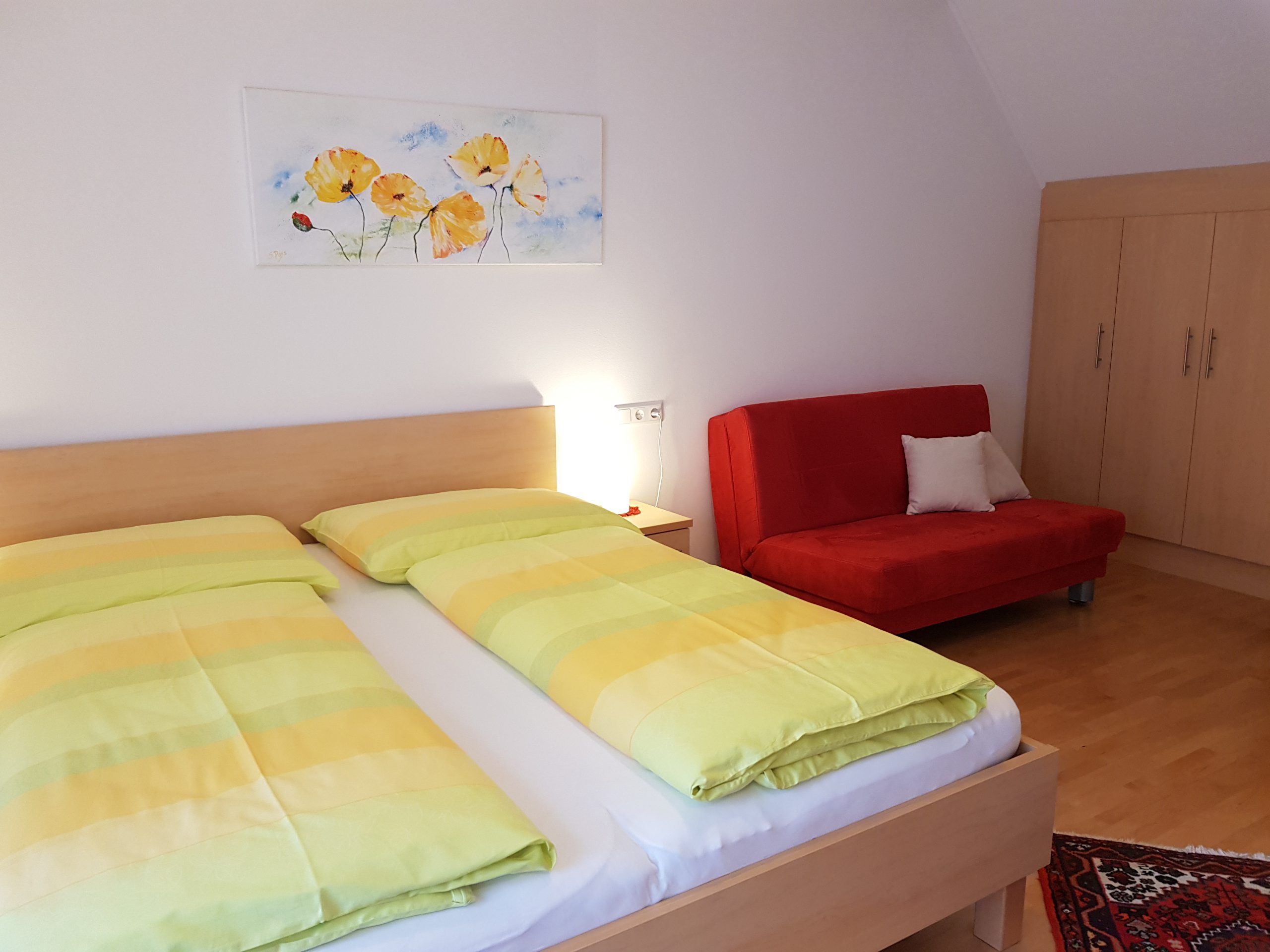 Ein Doppelzimmer mit einem Bett, einem roten Sofa, einem Schrank und einem Bild an der Wand.