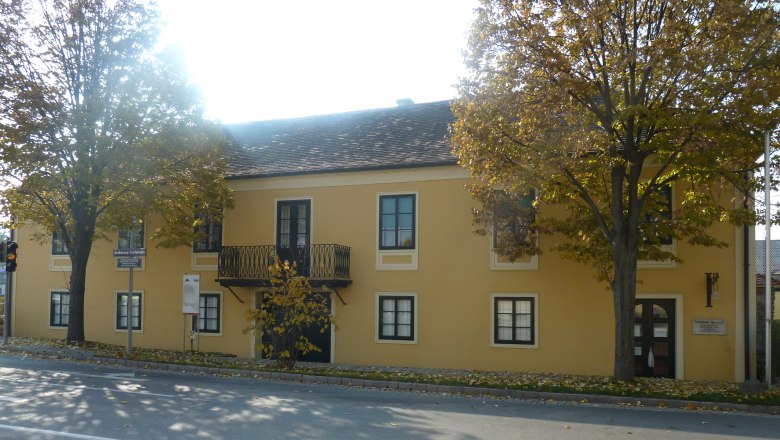 Gelbes Gebäude mit Balkon und Bäumen davor, Erzherzog Carl Haus und Napoleonmuseum in Deutsch-Wagram.