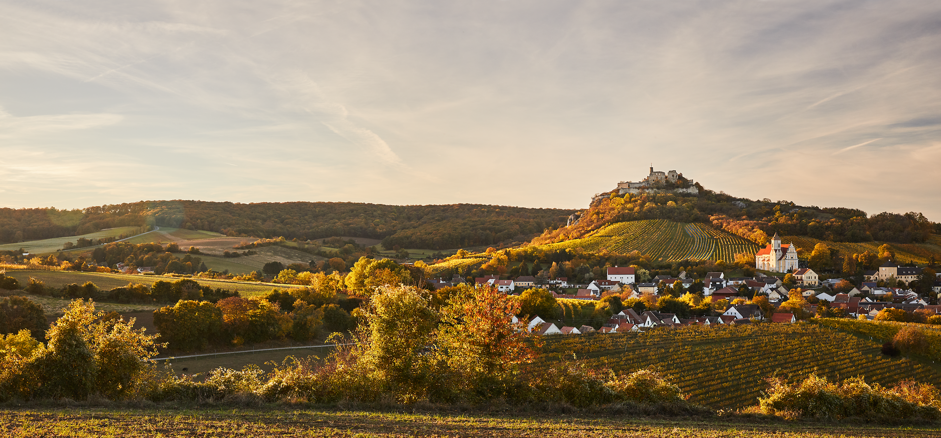 Die sanften Hügel und die goldenen Weinreben laden zu einem entspannenden Spaziergang ein. Die warmen Farben des Herbstes schaffen eine malerische Kulisse, während die sanfte Brise die Blätter zum Rascheln bringt. Ein perfekter Ort, um die Schönheit der Natur zu genießen und die Seele baumeln zu lassen.