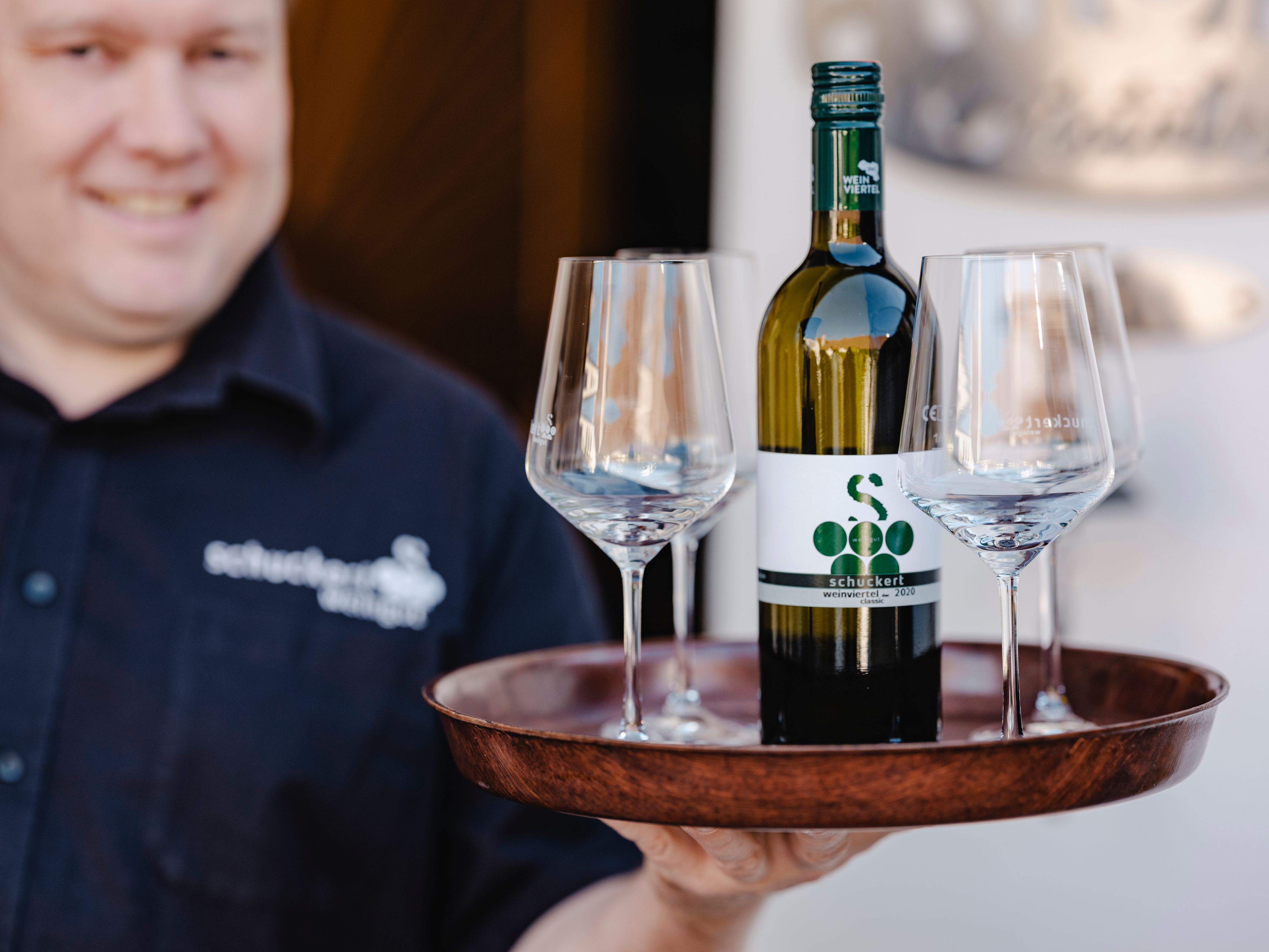 A man holds a tray with a bottle of wine and three glasses.