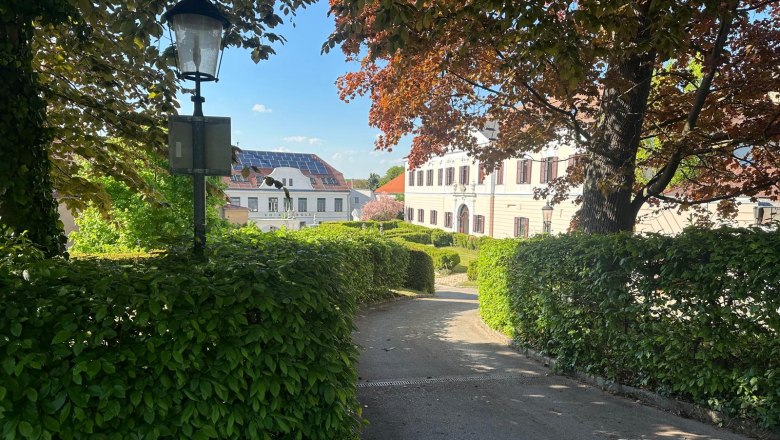 Schloßansicht aus Eigenwald, © smart concept team gmbh Ansicht eines Schlosses in Großrußbach, umgeben von Bäumen und Hecken, mit einer Laterne im Vordergrund.