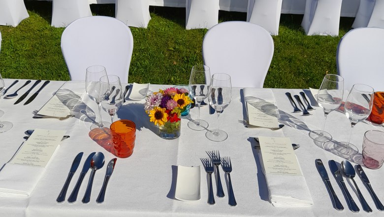 Festlich gedeckter Tisch im Freien mit weißen Tischdecken und Stuhlhussen.