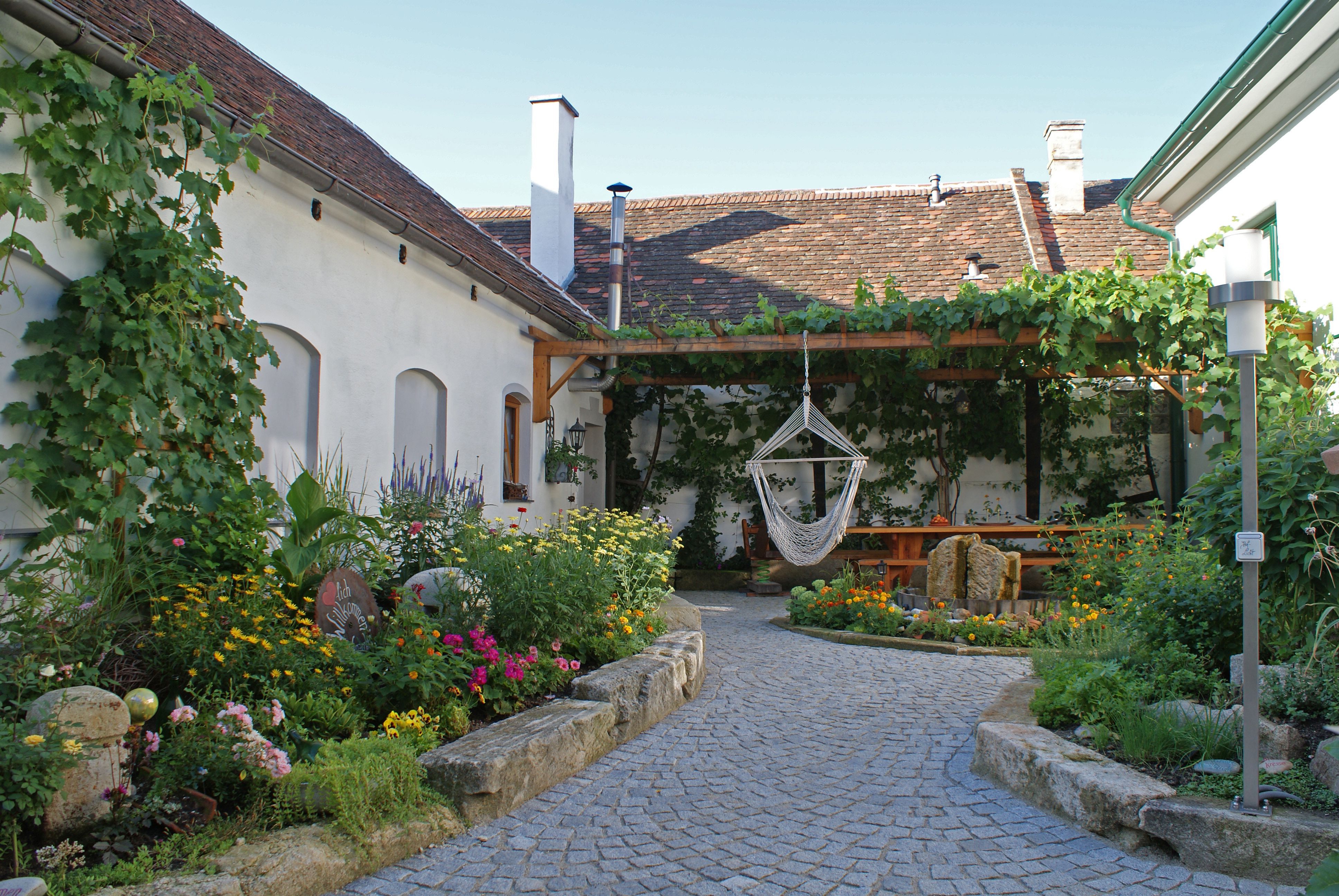 Ein idyllischer Innenhof mit Blumenbeeten, einer Hängematte und einem überdachten Sitzbereich.