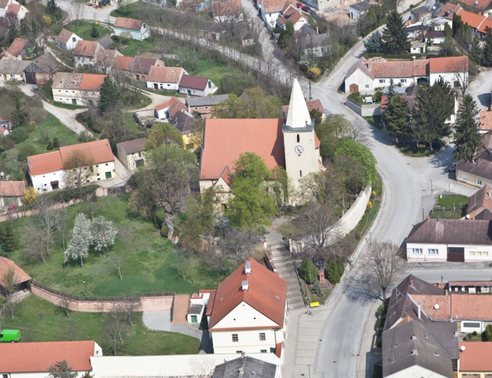 Luftaufnahme einer Kirche in einem Dorf mit umliegenden Häusern und Straßen.