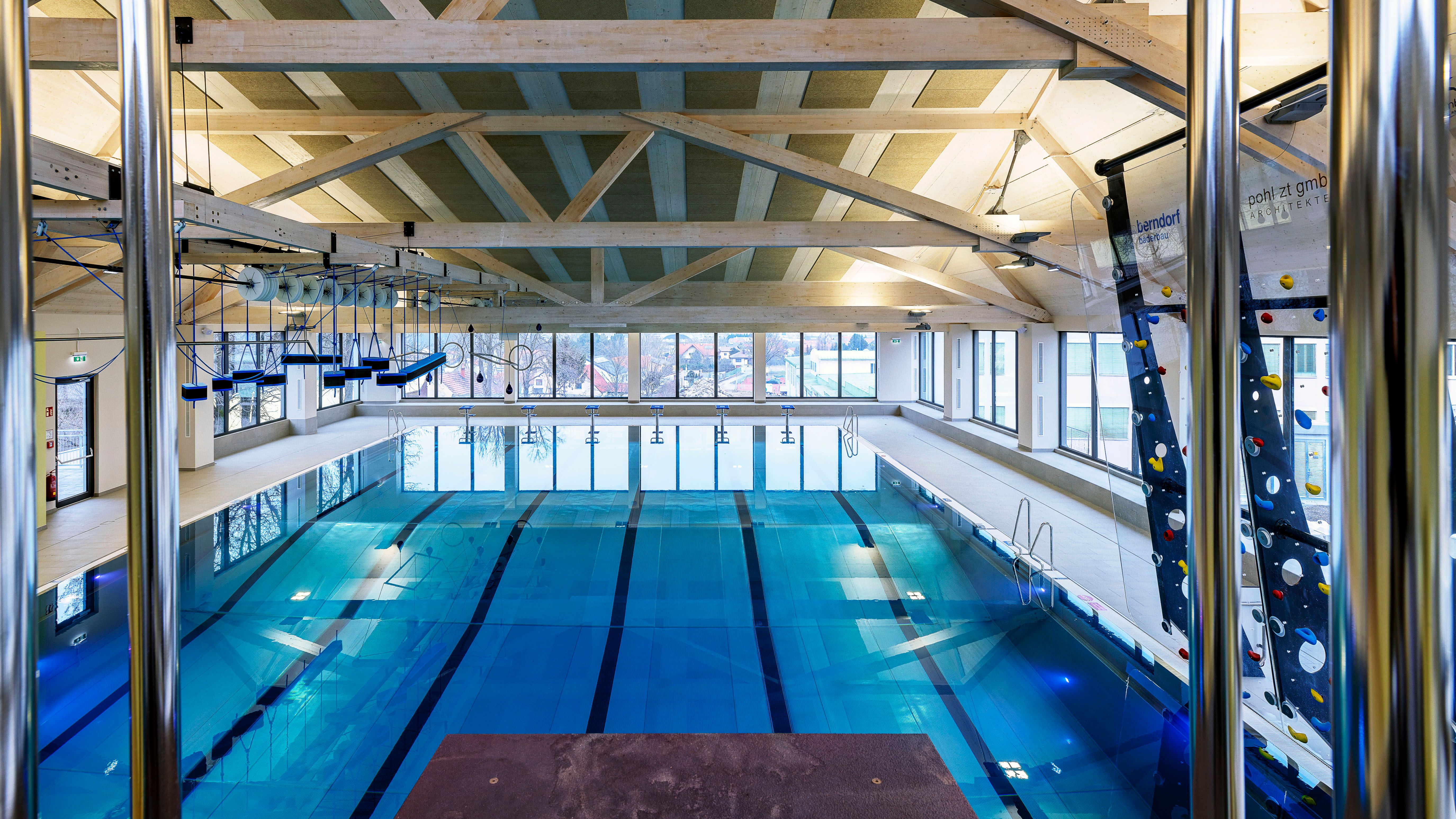 Innenansicht eines modernen Hallenbads mit Schwimmbahnen und Kletterwand.
