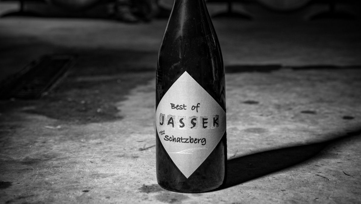 Black and white photo of a wine bottle with the label 'Best of Jassek Schatzberg' on a concrete floor.