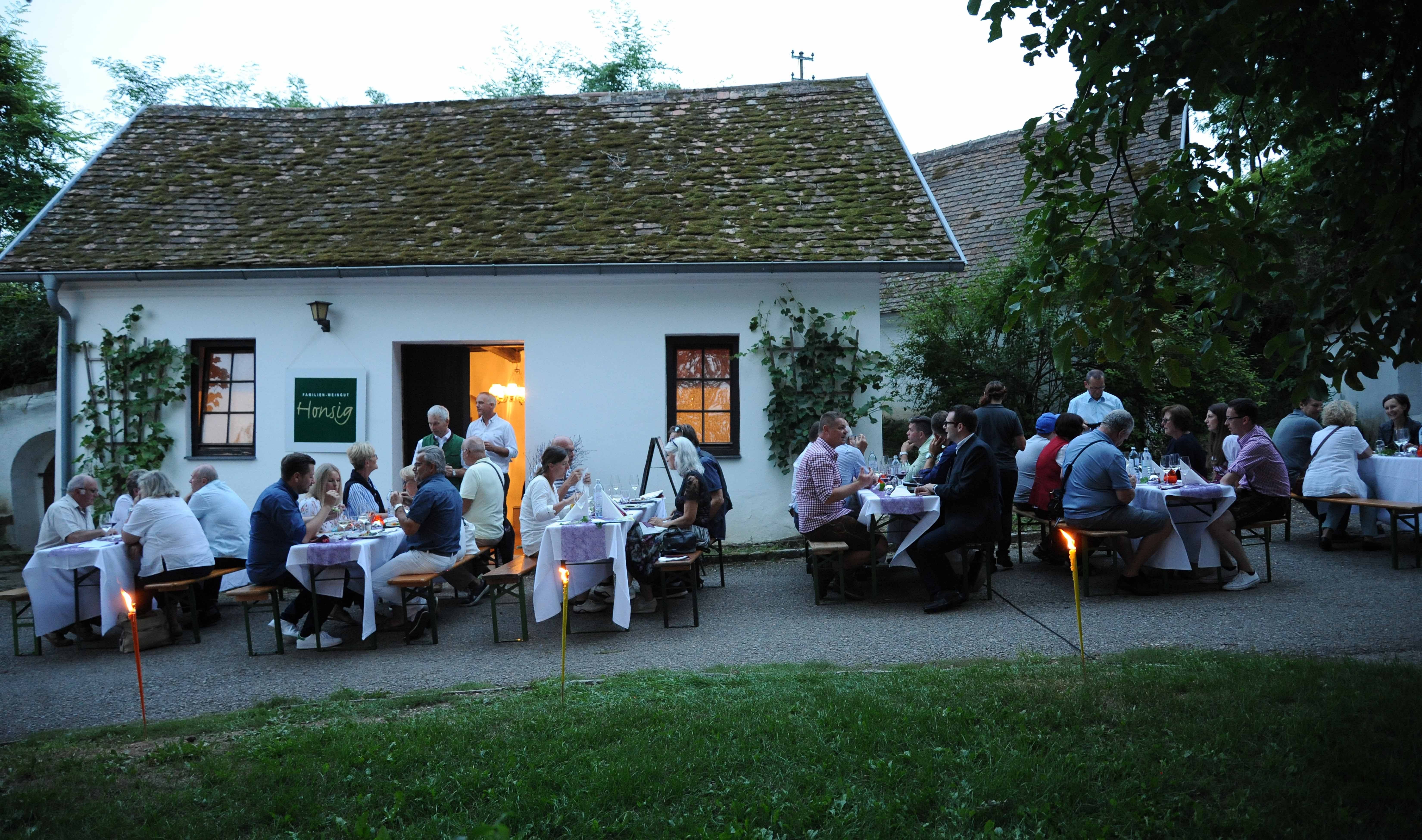 People sit in front of a wine cellar in the evening and enjoy a meal outdoors.