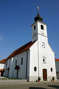 Weiße Kirche mit Turm und rotem Dach vor blauem Himmel.