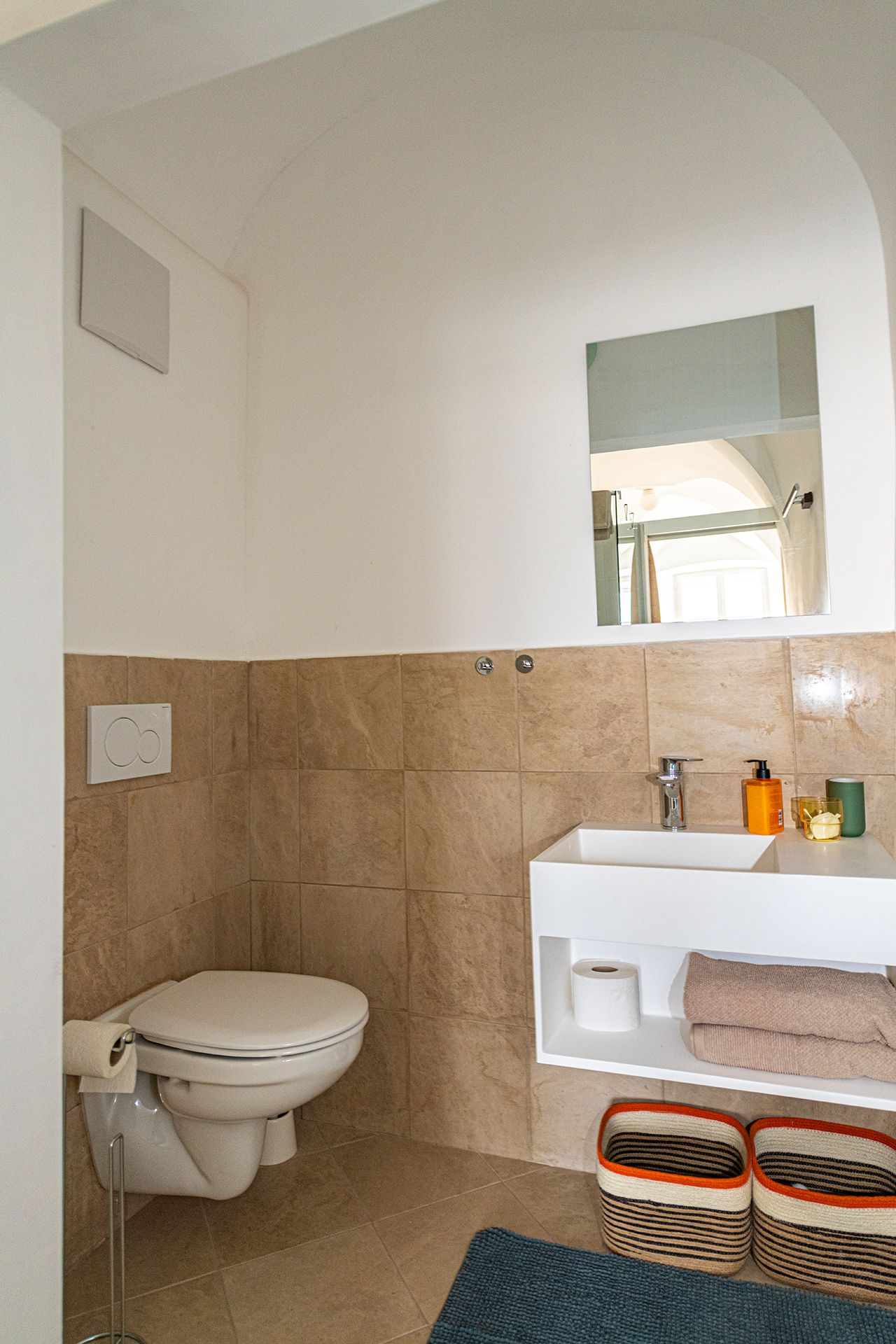 Modernes Badezimmer mit WC, Waschbecken, Spiegel und Ablageflächen.