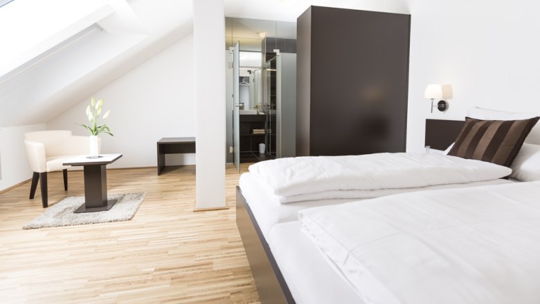 Modernes Gästezimmer mit Bett, Sessel und Tisch unter Dachschräge.