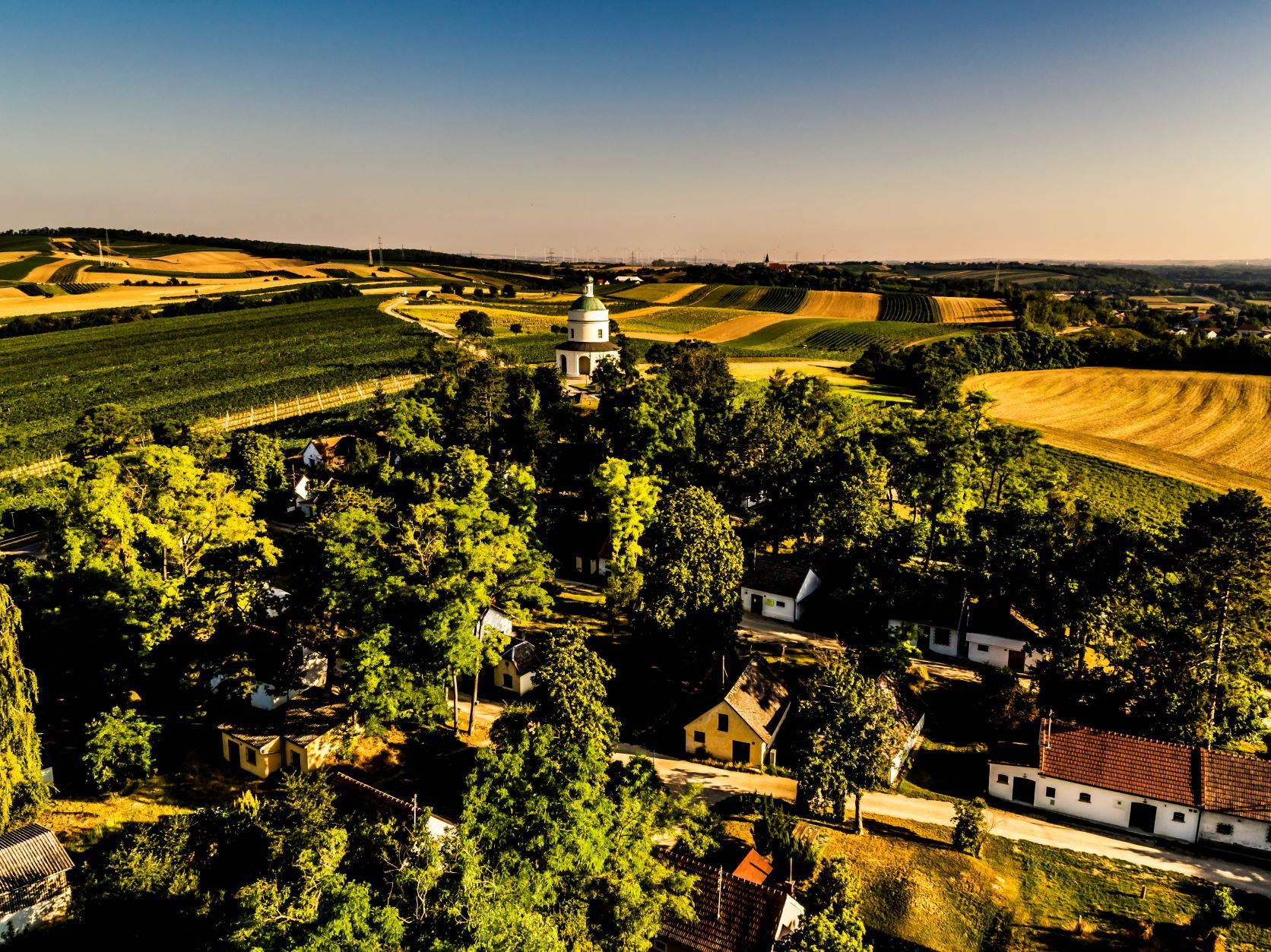 Landschaft mit Feldern, Bäumen und einer kleinen Kirche in der Mitte.