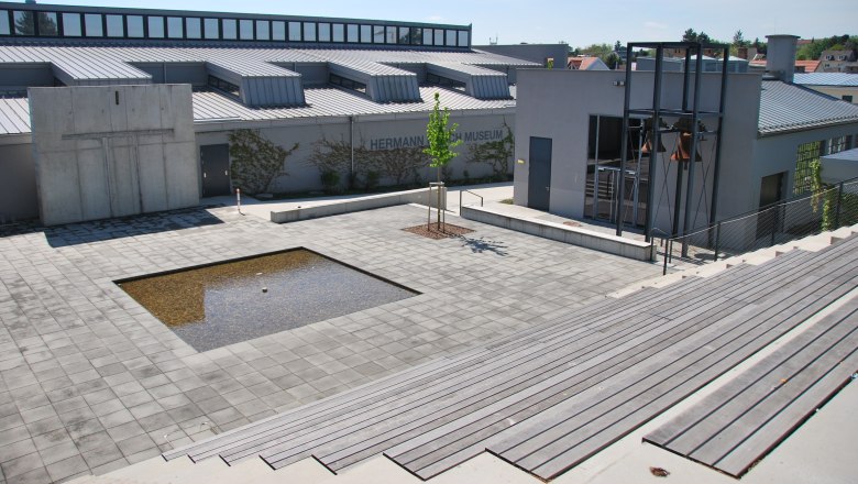 Au&szlig;enansicht des Hermann Nitsch Museums mit modernem Design und einem kleinen Wasserbecken auf der Piazza.