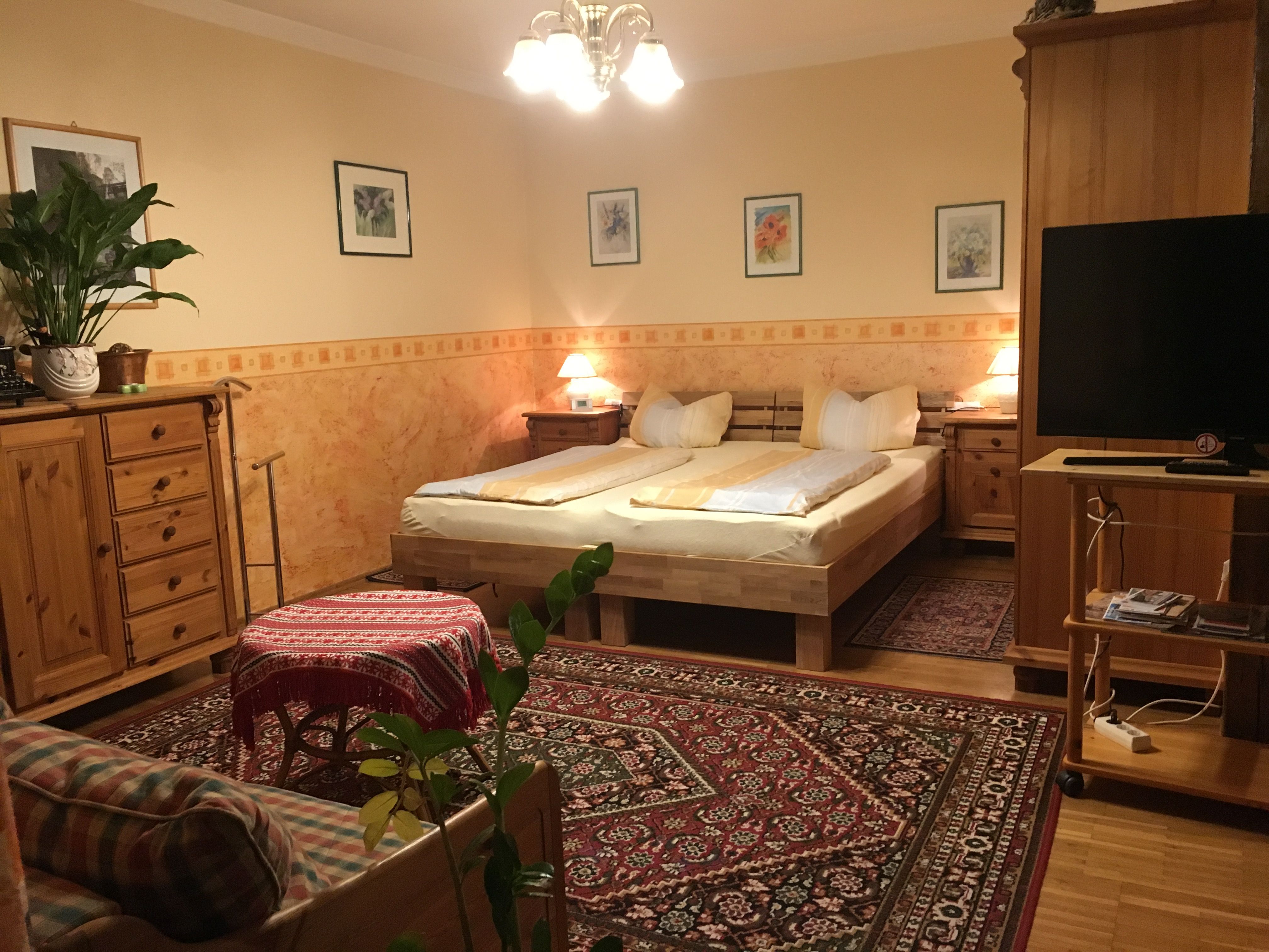 Gemütliches Schlafzimmer mit Holzmöbeln, Doppelbett, Teppich und Pflanzen.