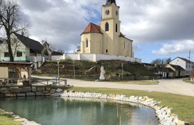 Kirche in Glaubendorf mit Teich im Vordergrund.