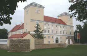 Schloss Wolkersdorf mit zwei Türmen und einem runden Steinturm im Vordergrund.