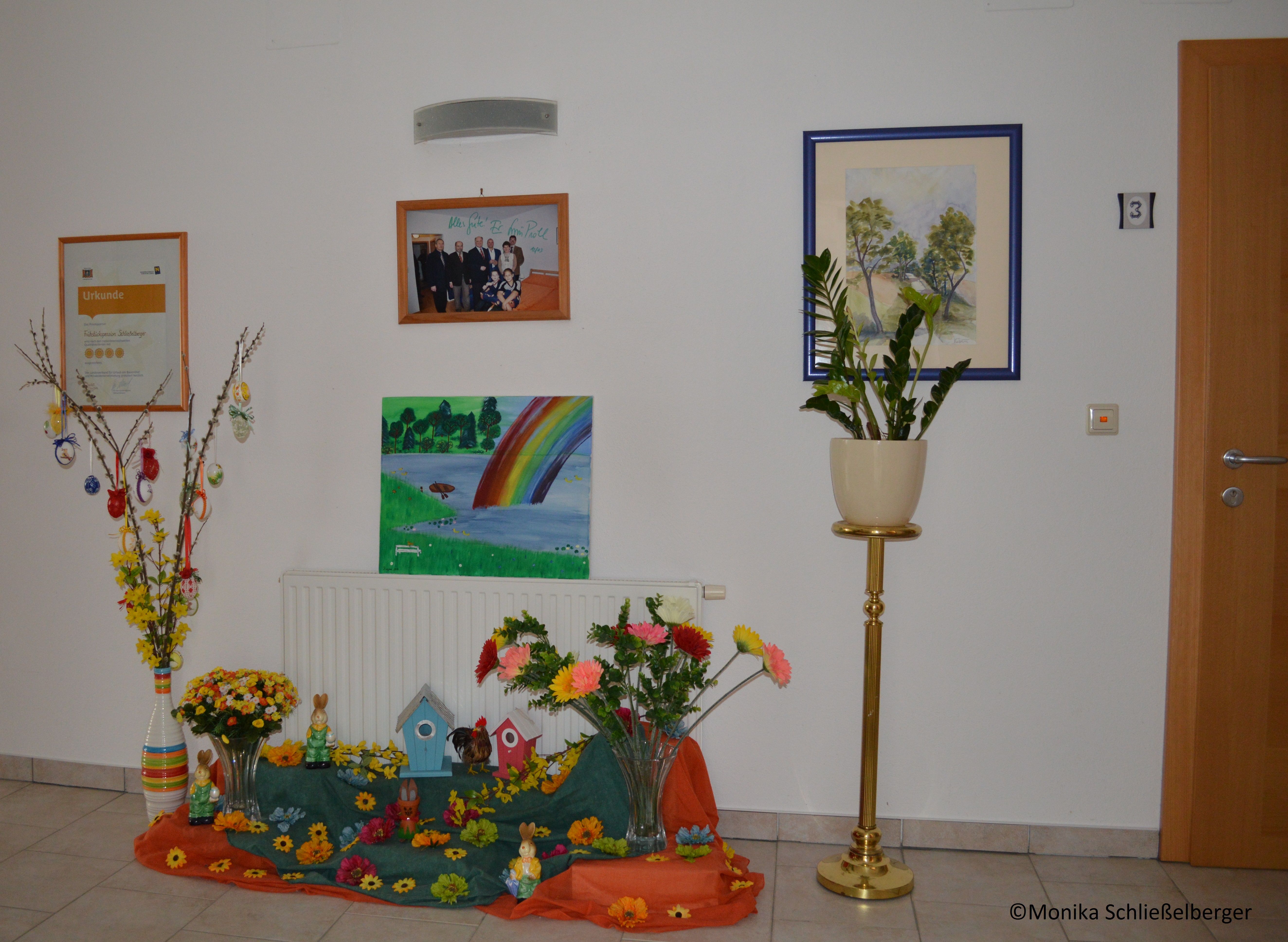 Dekorierter Eingangsbereich mit Bildern, Pflanzen und Osterdekoration.