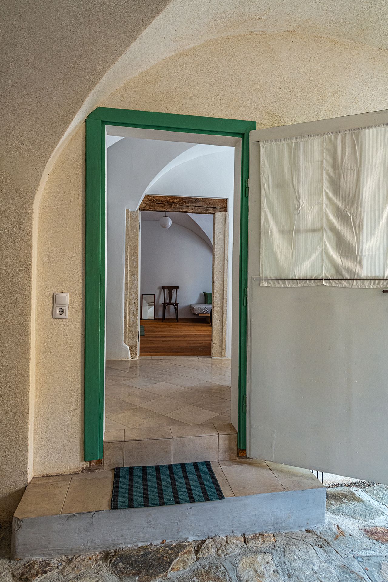 Blick durch eine geöffnete Tür in ein Gewölbezimmer mit Holzboden und einem Stuhl.