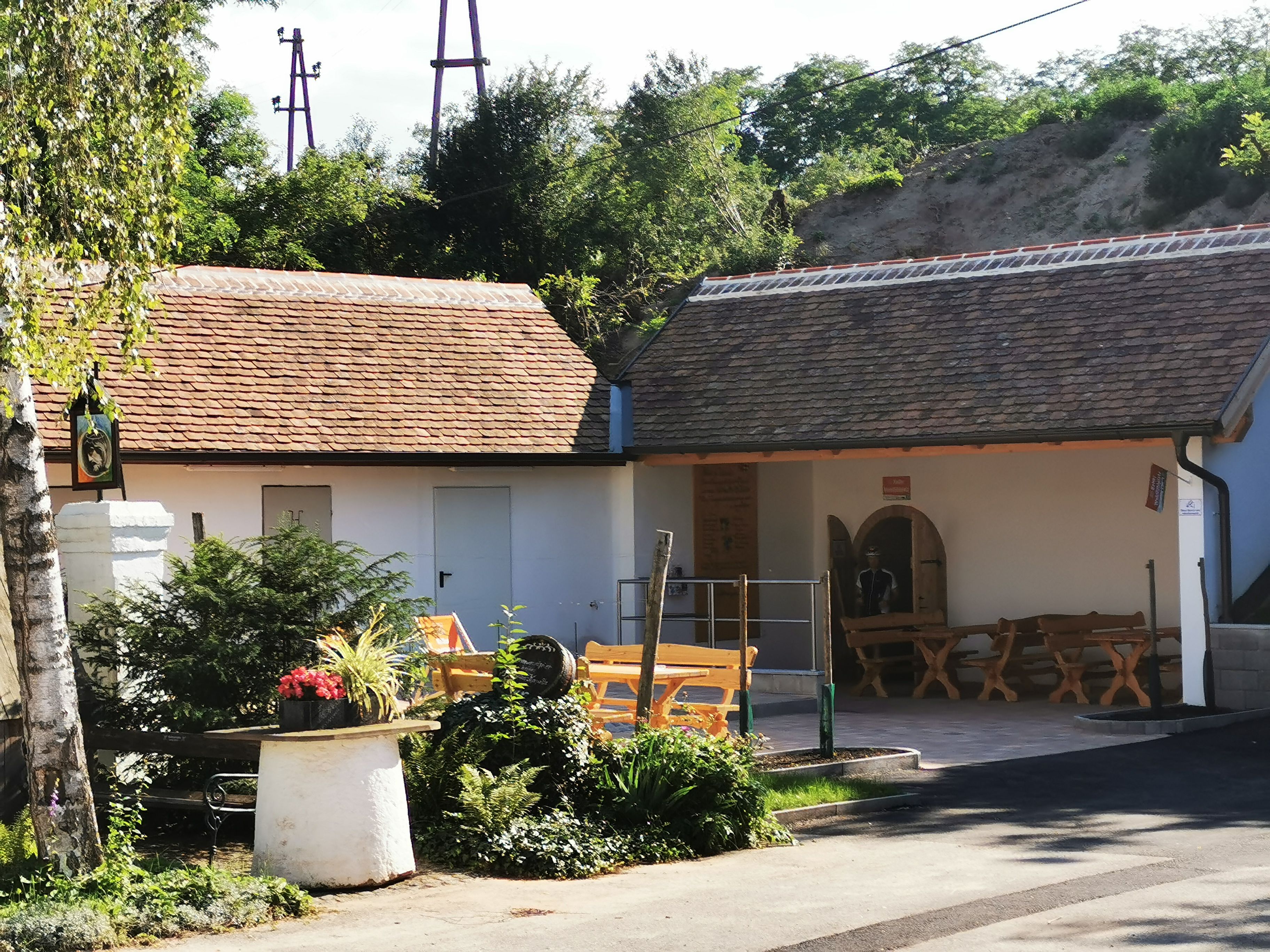 A cozy outdoor area with wooden benches and plants in front of a building with a tiled roof.