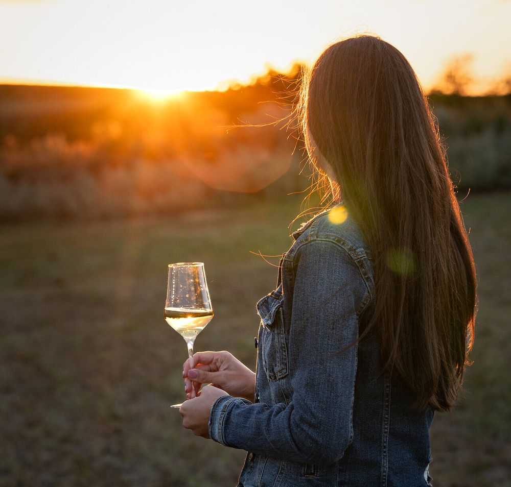 Eine Frau genießt mit einem Glas Weißwein in der Hand den Blick auf den Sonnenuntergang.