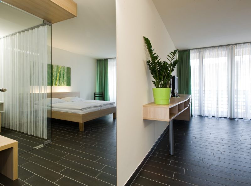 Modernes Hotelzimmer mit Doppelbett, grünem Vorhang und Zimmerpflanze.