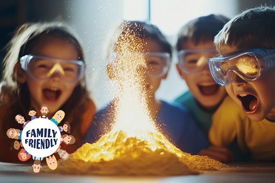 Begeisterte Kinder mit Brillen vor einem dramatischen Vulkanausbruchsexperiment. | family