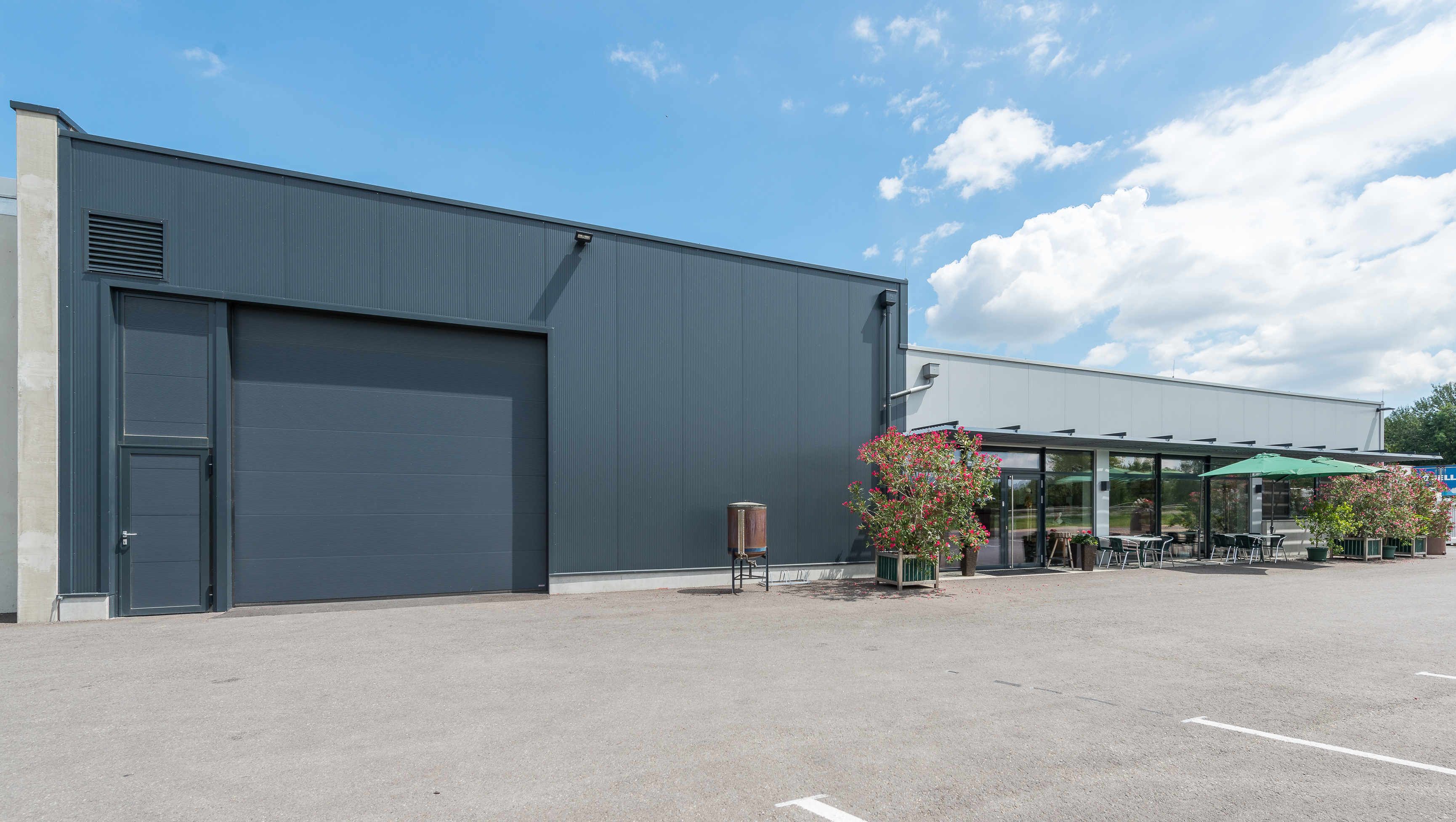 Moderne Industriehalle mit Glasfront und Terrasse mit Sonnenschirm.
