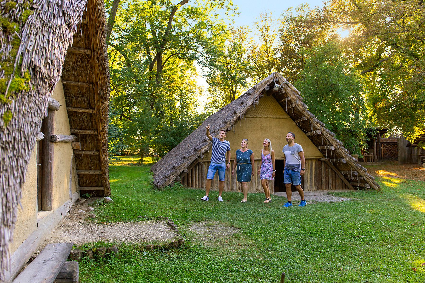 Four people stand outside a historic building with a thatched roof.