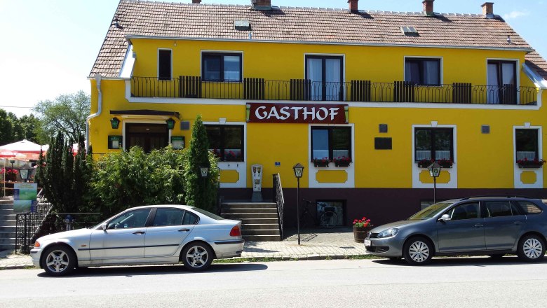 Gelbes Gebäude mit der Aufschrift 'Gasthof', zwei geparkte Autos davor.