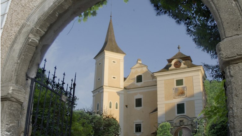 Schloss Mühlbach hinter einem steinernen Torbogen mit schmiedeeisernem Tor.
