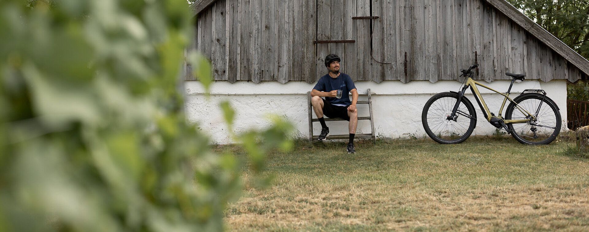In der malerischen Umgebung von Pillersdorf lädt eine ruhige Bank zum Verweilen ein. Umgeben von sanften Hügeln und üppigem Grün, genießen Radfahrer die friedliche Atmosphäre und die Schönheit der Natur. Die charmante Holzhütte im Hintergrund erzählt von der traditionellen Weinbaukultur der Region.
