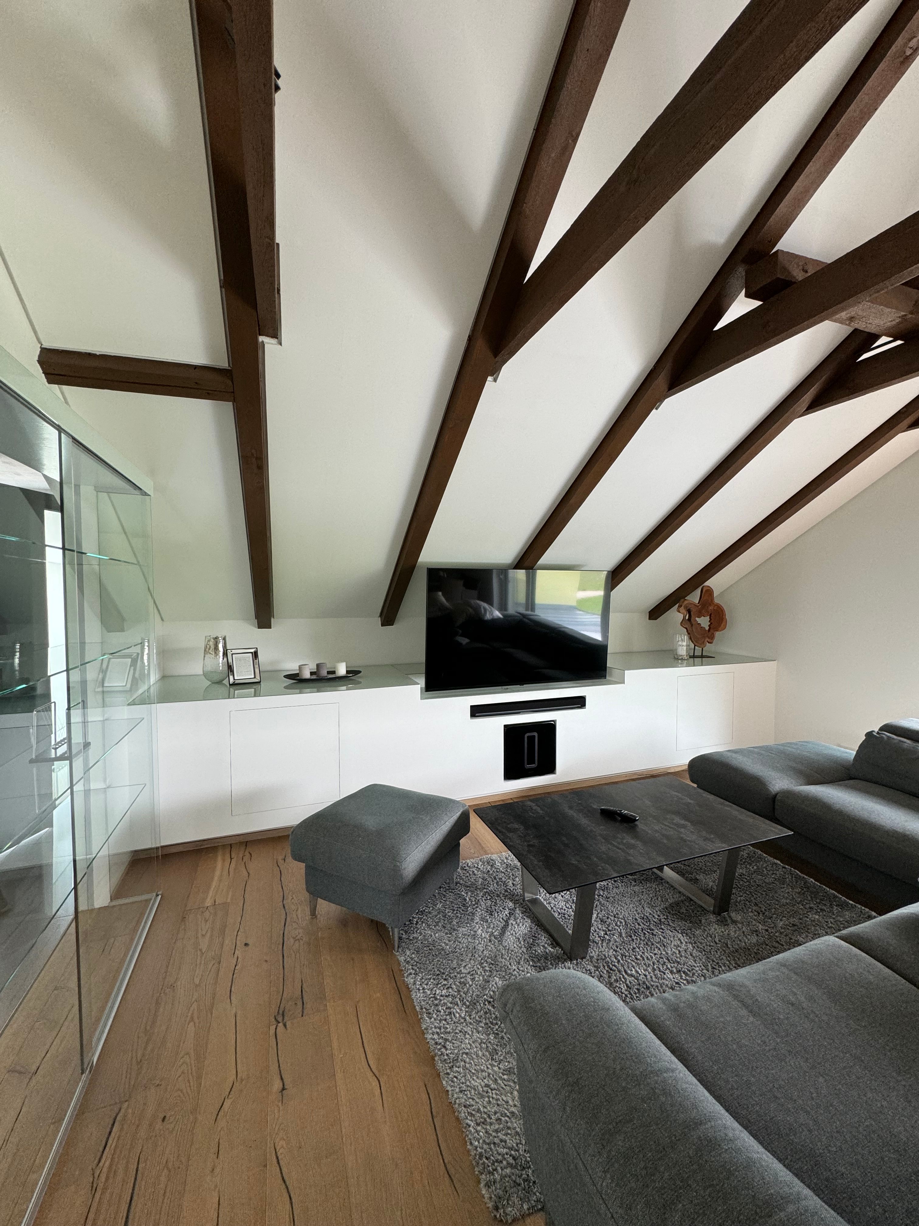 Moderner Wohnbereich mit grauem Sofa, Holzbalkendecke und Flachbildfernseher.