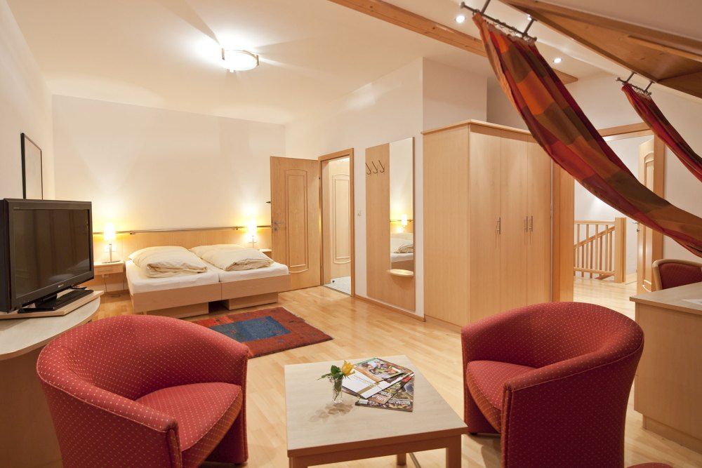 Gemütliches Gästezimmer mit Doppelbett, TV, roten Sesseln und Hängematte.