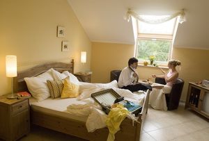 Ein gemütliches Hotelzimmer mit einem Paar, das am Tisch sitzt. Das Bett ist ungemacht und ein Koffer liegt offen auf dem Bett.