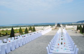 Langer, festlich gedeckter Tisch im Schlosshof mit Garten und Skulpturen im Hintergrund.