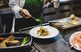 Koch dekoriert ein Gericht mit Kräutern in einer Küche.