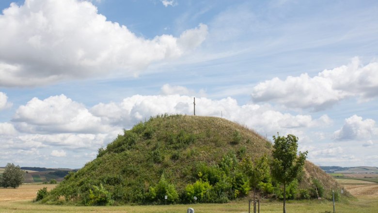Ein grasbewachsener Hügel mit einem Kreuz auf der Spitze unter einem bewölkten Himmel.