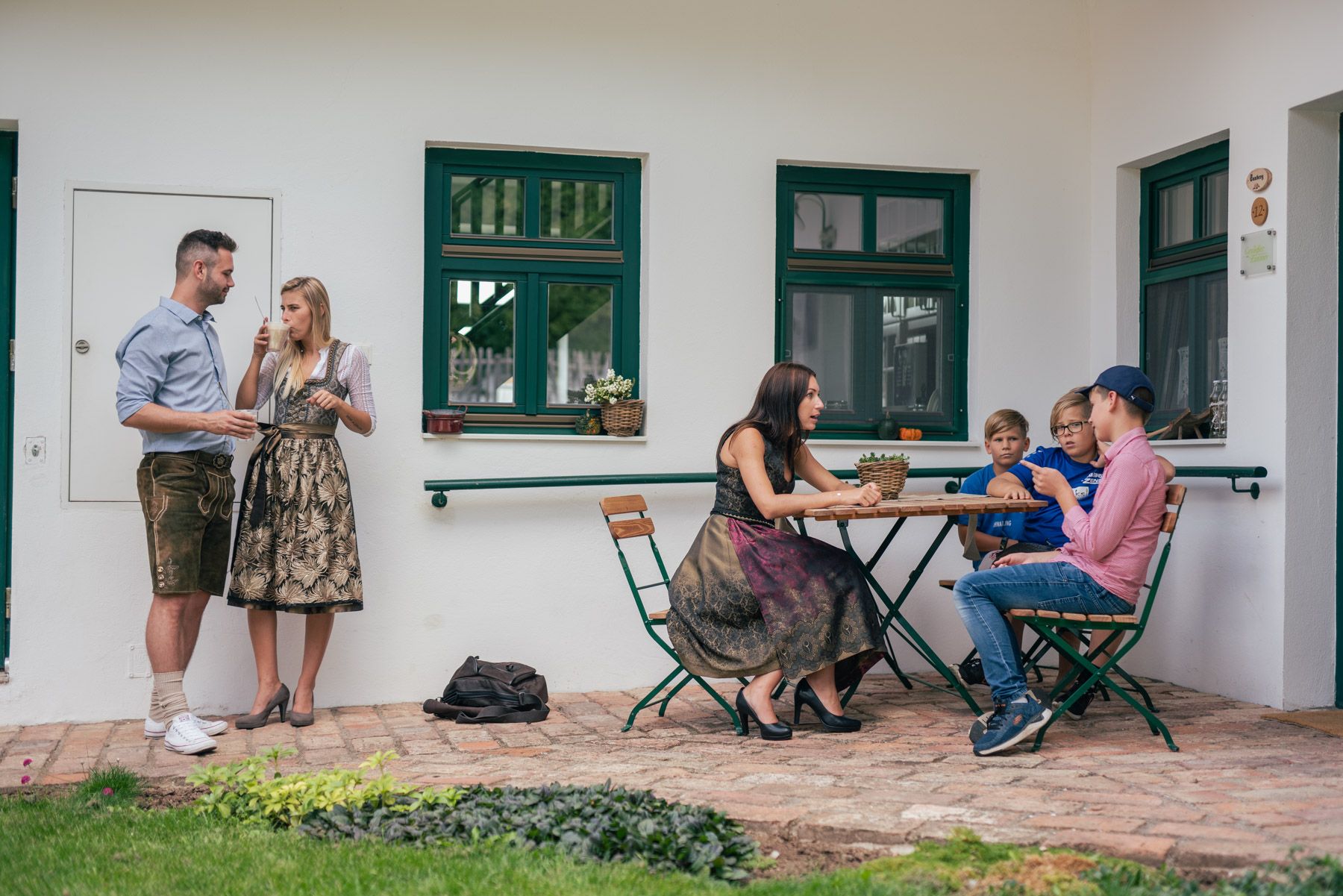 Menschen in traditioneller Kleidung auf einem Winzerhof, einige stehen, andere sitzen an einem Tisch.