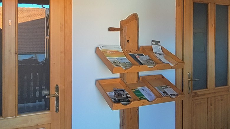 Ein Holzregal mit Prospekten an einer weißen Wand zwischen zwei Holztüren.