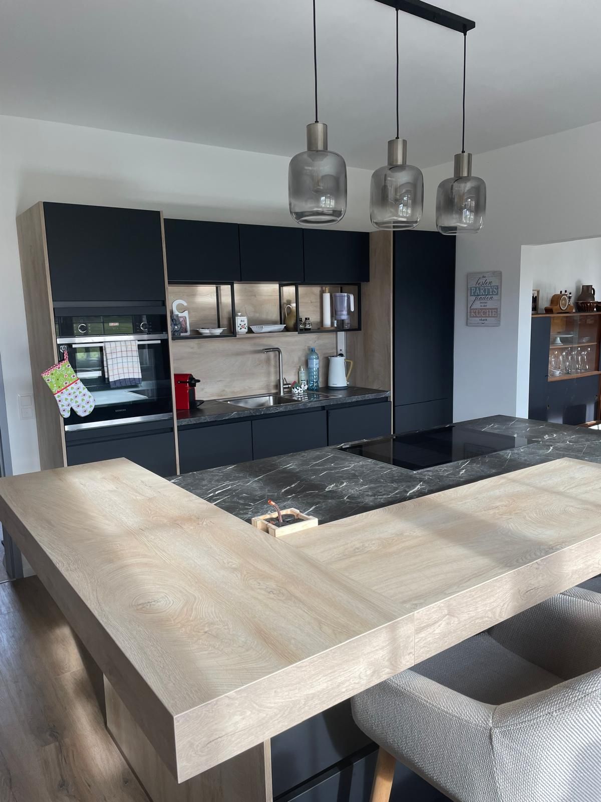 Moderne Küche mit Holz- und Marmorelementen, drei Hängelampen und schwarzen Schränken.