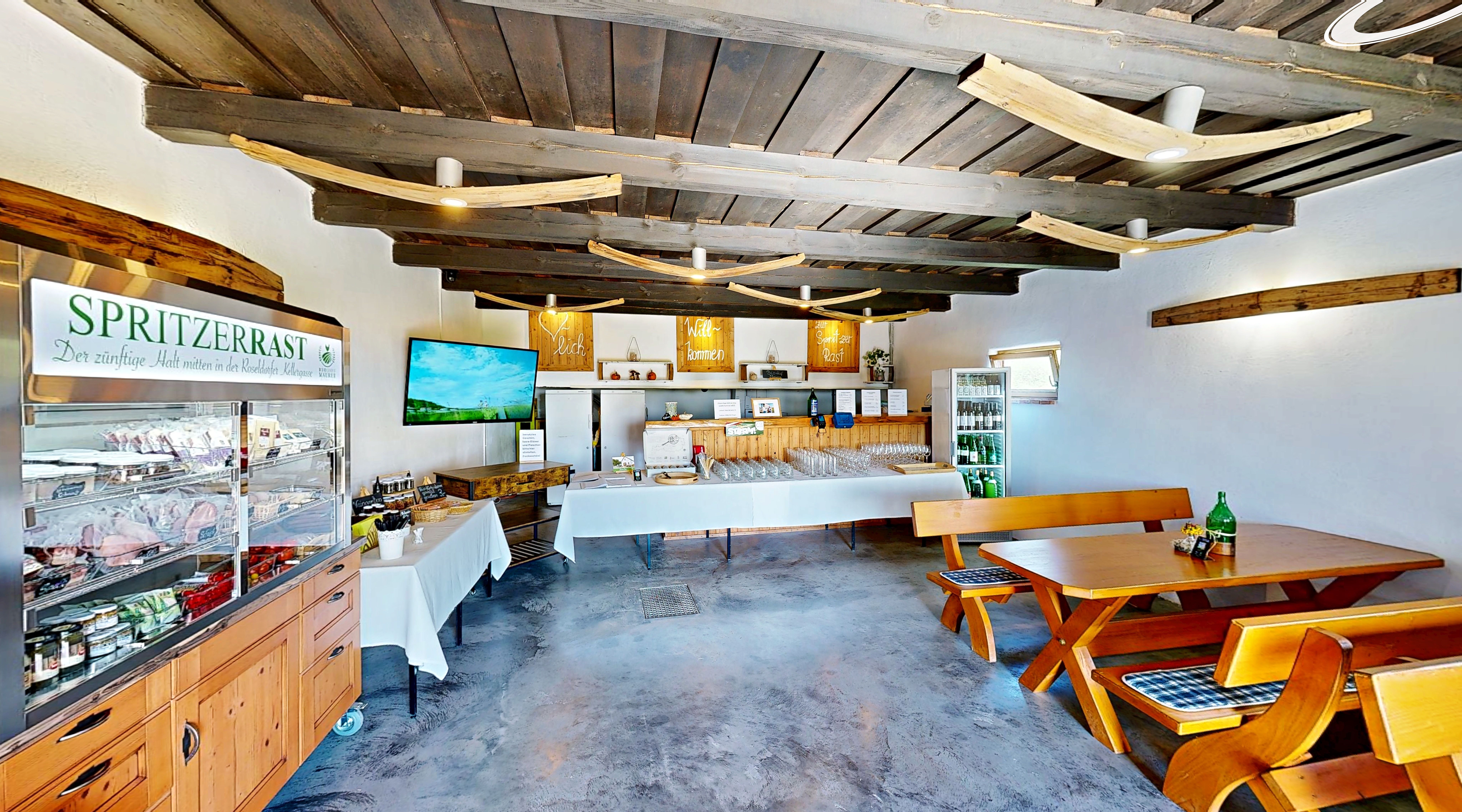 Innenansicht eines rustikalen Gastraums mit Holzmöbeln und einem Kühlschrank voller Getränke.