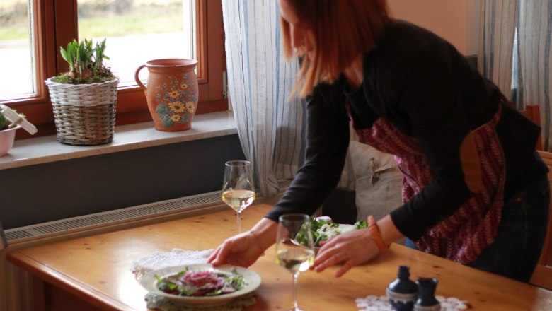 A woman sets a table with salad and white wine.