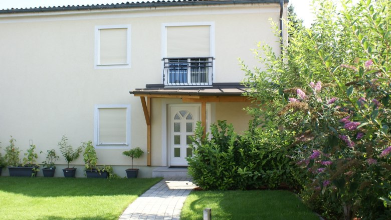 Exterior view of Pension Wagram, © © Pension Wagram Exterior view of a two-story house with garden and plants.