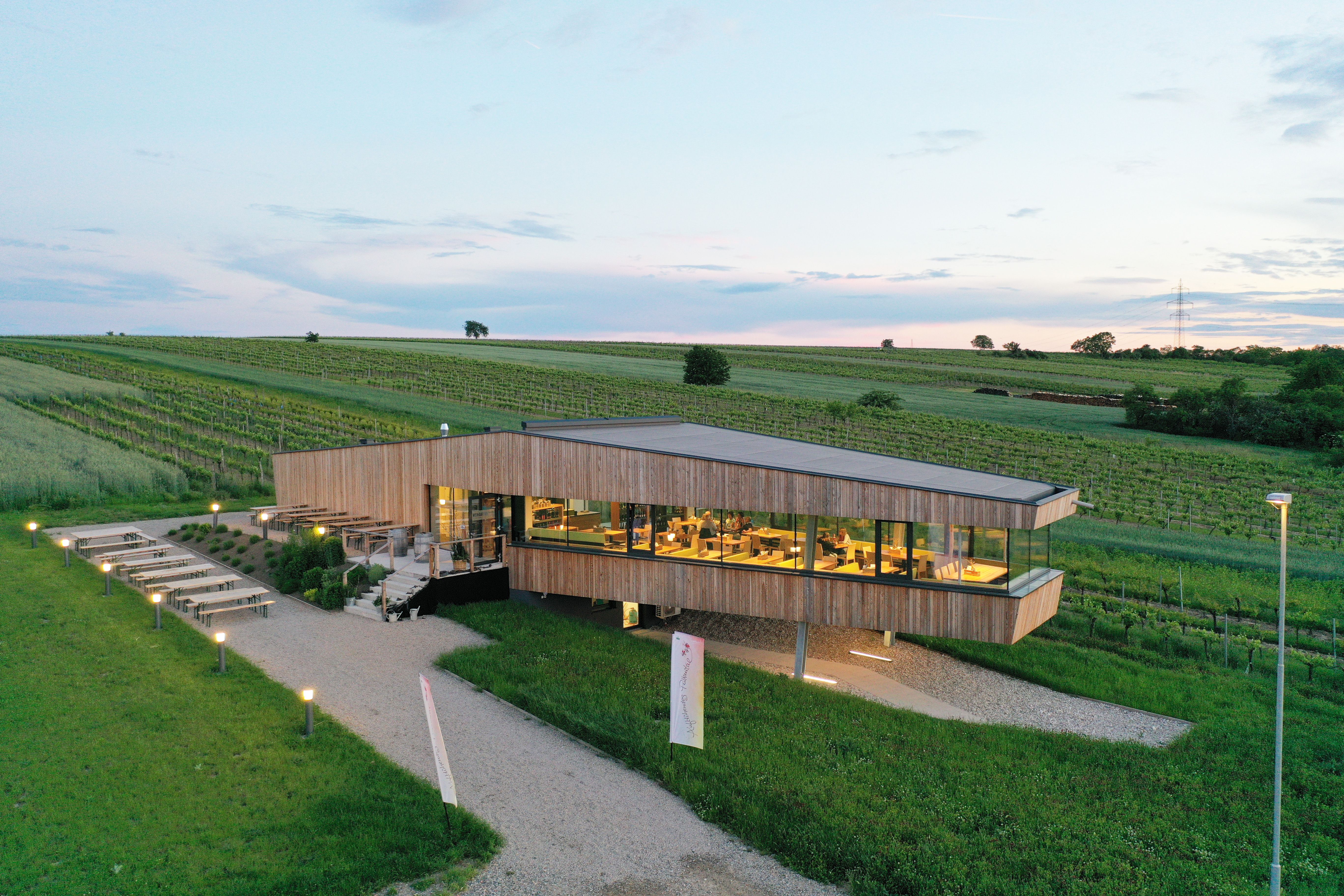 Modernes Gebäude inmitten von Weinbergen bei Sonnenuntergang.