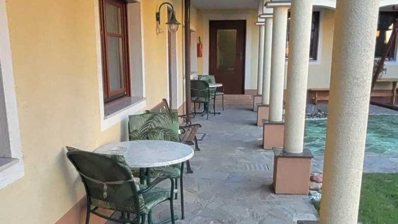 Ein Arkadenhof mit Steinboden, gelber Wand und Säulen. Tische und Stühle stehen entlang der Wand.