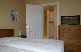 Ein gemütliches Doppelzimmer mit Bett, Kommode, Bücherregal und offenem Bad.