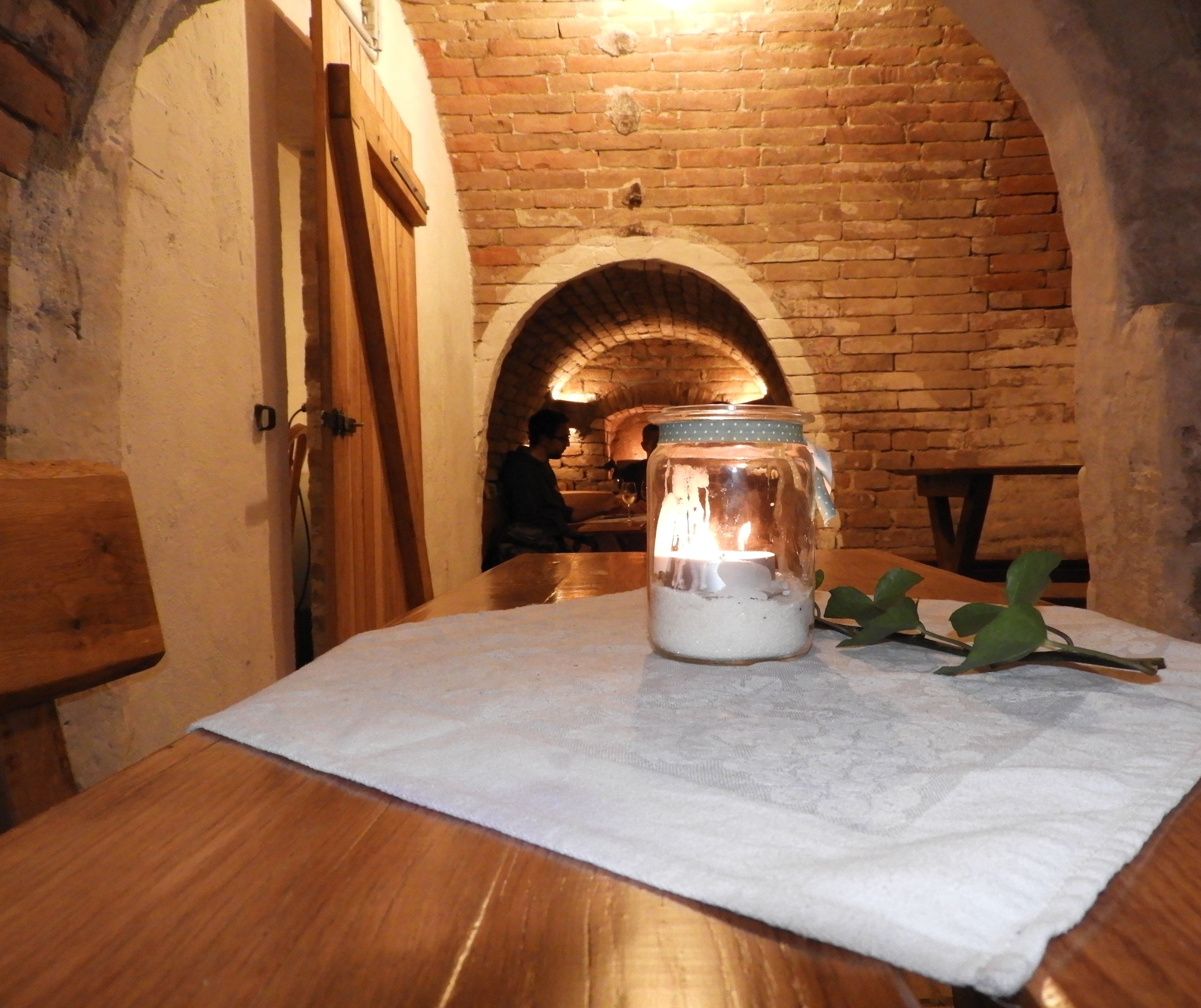 A cozy wine cellar with a candle on a table, brick walls and a vaulted ceiling.