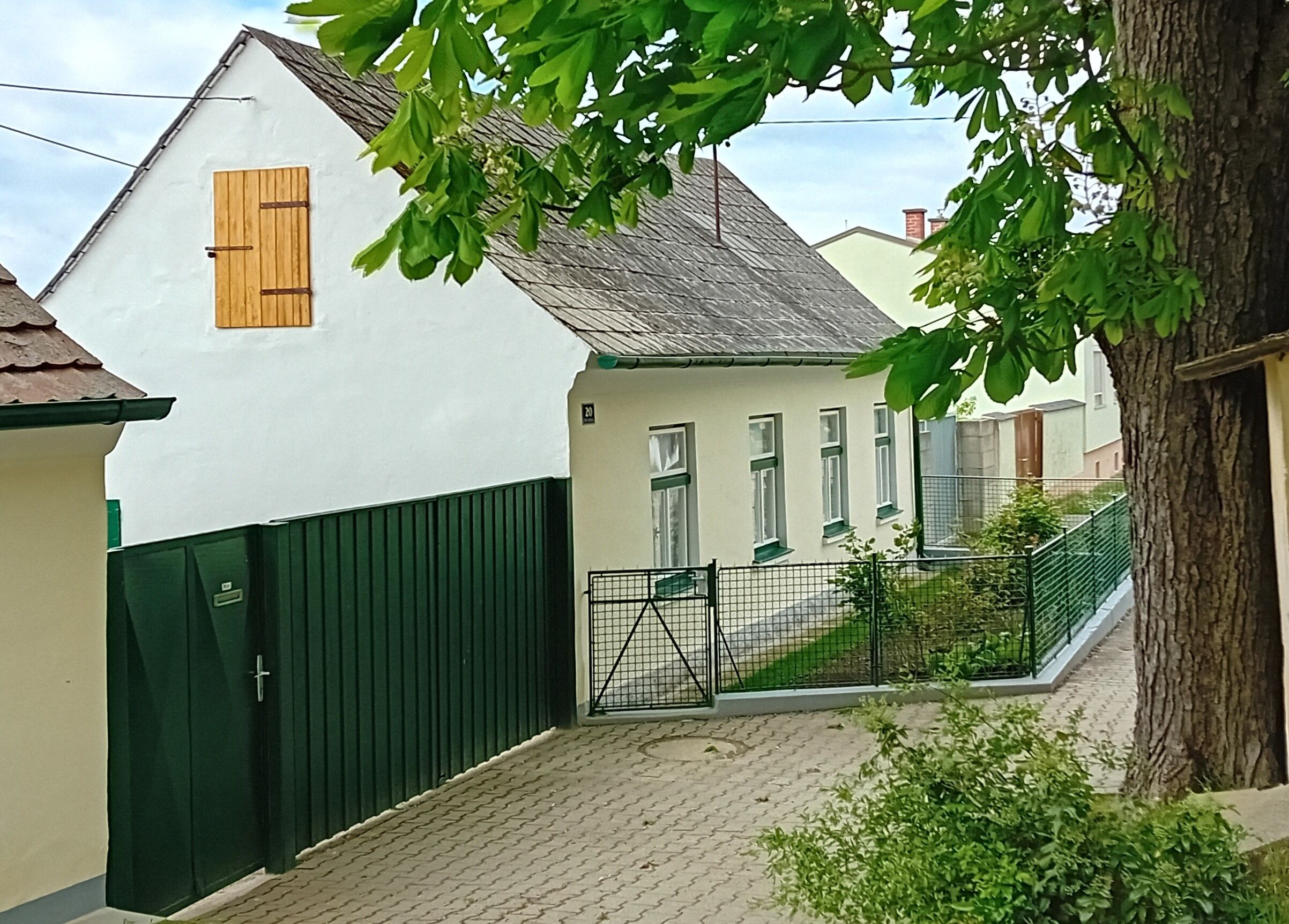 Ein traditionelles, weißes Ferienhaus mit grünem Zaun und Baum im Vordergrund.